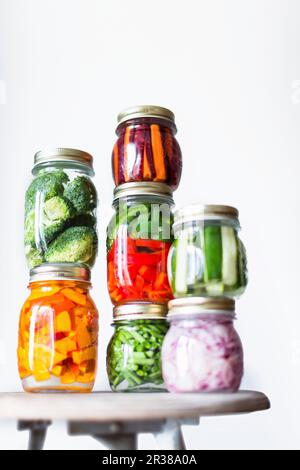 Preserving jars of freshly pickled vegetables stacked on an old stool Stock Photo
