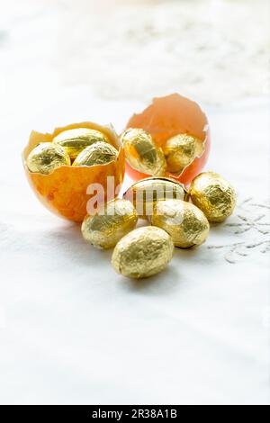A dyed egg shell of an empty Easter egg filled with chocolate eggs wrapped in gold foil Stock Photo