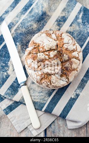 A loaf of homemade sourdough bread on a cloth next to a bag of flour and a knife Stock Photo