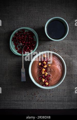 Vegan banana and peanut smoothie bowl with pomegranate seeds, dried apple and flaxseeds Stock Photo