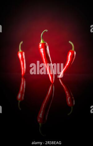 Three chilli peppers against a black and red background Stock Photo