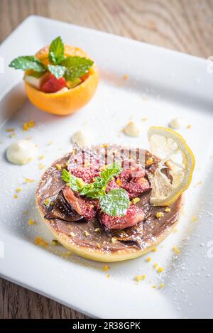 Fresh shortcrust pastry tart with a chocolate and orange mousse and figs decorated with citrus peel and icing sugar and mint Stock Photo