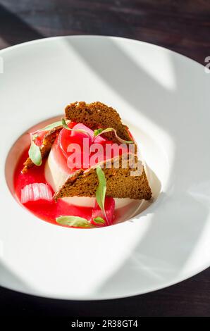 Rhubarb panna cotta with crispy waffles and a rhubarb sauce in a white plate on a dark background Stock Photo