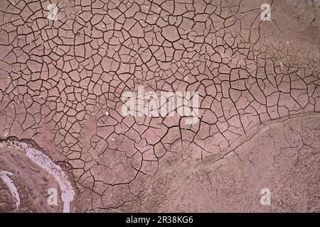 Top drone view on cracked dry soil on the river or sea bottom with a thin small creek of water still flowing. Drought and water shortage. Stock Photo