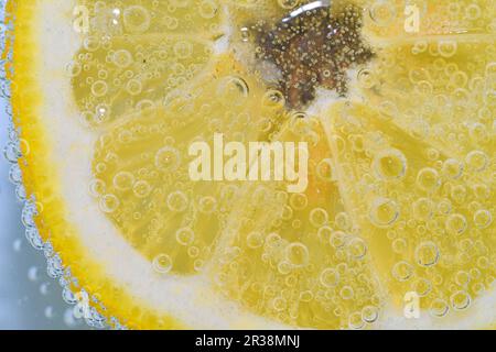 Close-up of a lemon slice in liquid with bubbles. Slice of ripe lemon in water. Close-up of fresh citron slice covered by bubbles. Macro horizontal Stock Photo
