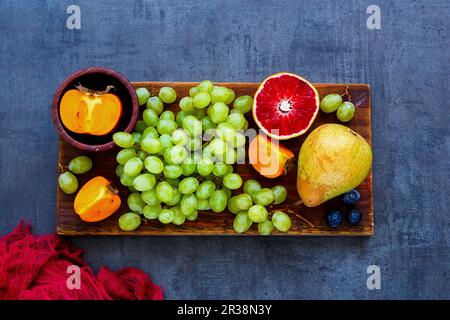 Selection of colorful organic fruit on rustic wooden chopping board over slate background Stock Photo