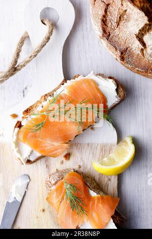 Two slices of bread with cream cheese, salmon and dill on a wooden board Stock Photo