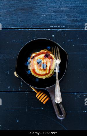 Top view of blueberries homemade pancakes with honey and fresh berries for breakfast in vintage cast iron pan over rustic wooden background Stock Photo