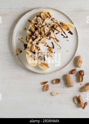 Halved bananas with peanuts, peanut butter and chocolate Stock Photo