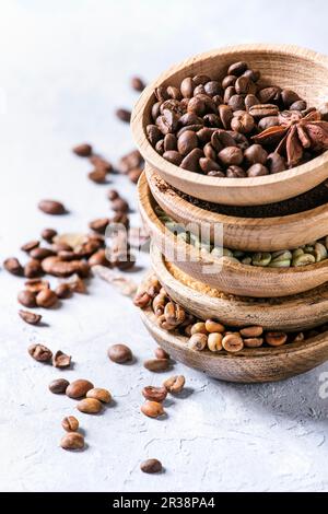 Variety of different coffee beans and spices in wooden bowls in stack over grey table Stock Photo