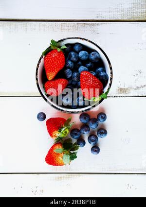 Blueberries and strawberries in a bowl and on a wooden surface (seen from above) Stock Photo