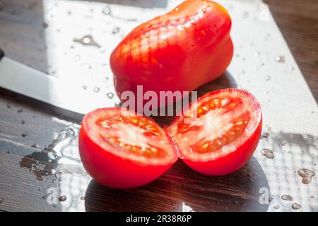 One whole and one halved tomato on a sunny outdoor table Stock Photo