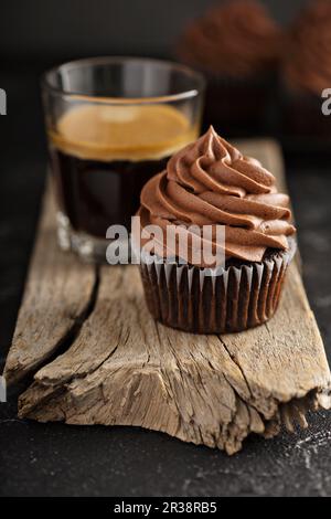Dark chocolate cupcakes with ganache frosting on dark background with espresso in a glass Stock Photo