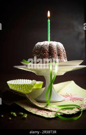 A mini chocolate cake with a candle on a cake stand Stock Photo