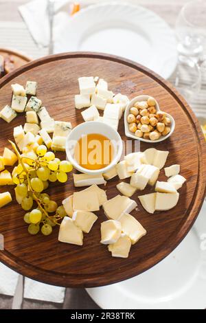 Cheese plate with hazelnuts, honey, grapes on wooden table Stock Photo