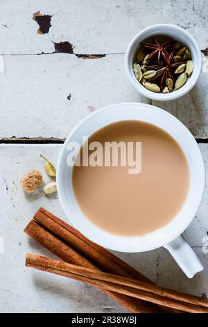Grunge wooden table with traditional Indian masala tea in white ceramic cup and spices (cinnamon, anise, cardamom, sugar) Stock Photo
