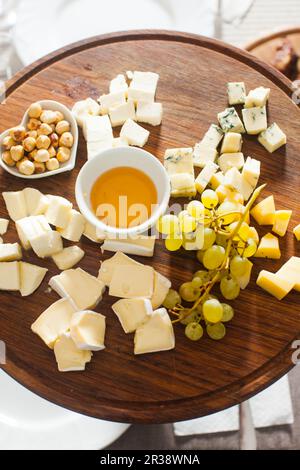 Cheese plate with hazelnuts, honey, grapes on wooden table Stock Photo