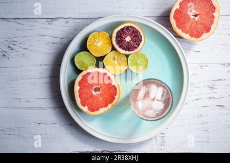 Halved citrus fruits, a glass of grapefruit infused water with ice on a blue plate Stock Photo
