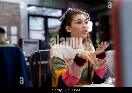 Busy diverse businesswoman working at desks using smartphone in creative office, unaltered Stock Photo