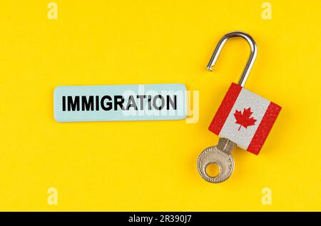 On a yellow surface, an open lock with the image of the flag of Canada with a key and a sticker with the inscription - immigration Stock Photo