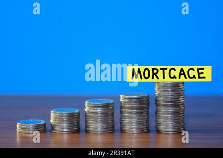 A row of a growing stack of coins illustrating increasing mortgage rates due to the rising cost of living, on a blue background with copy space Stock Photo