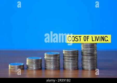 A row of a growing stack of coins illustrating the rising cost of living, on a blue background with copy space at the top, concept Stock Photo