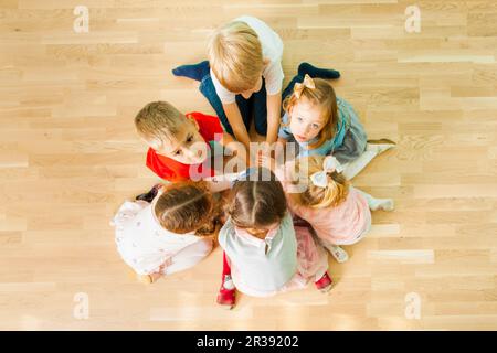 Six kids sitting in a circle with their hands together Stock Photo