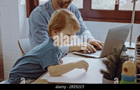 Father working from home office using laptop sit at table with cute little son playing nearly to disturb. Stock Photo