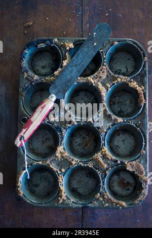 An empty muffin tins with cake crumbs and a palette knife Stock Photo