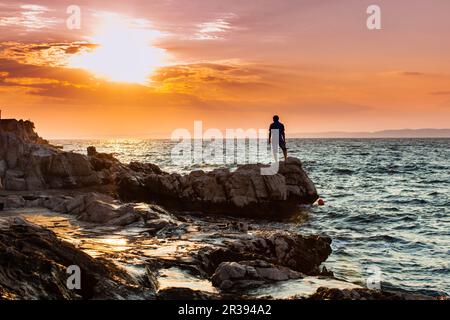 Yung man standing on a rock and looking at the sea sunset Stock Photo