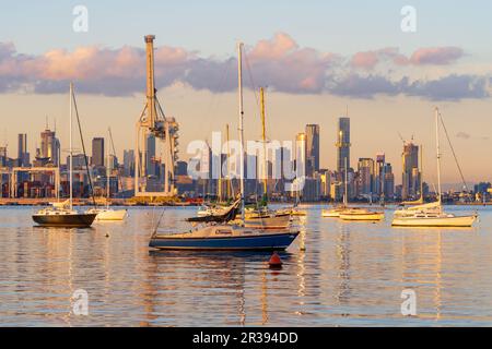 Yachts anchored on a calm coastal bay in front of cranes and city buildings on the distance at Port Melbourne in Victoria, Australia. Stock Photo