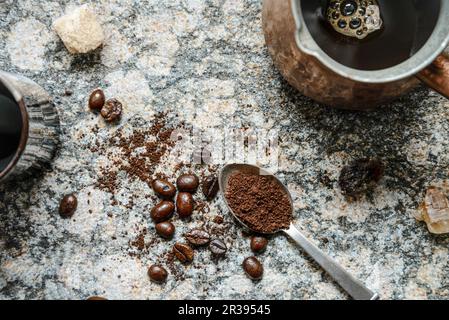 Top down view of scattered coffee beans, ground coffee in a spoon, brewed coffee in jezva on a granite surface Stock Photo