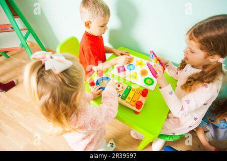 Toddler boy and girls sitting at the table in playroom. Stock Photo