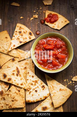 Small bowl and tomato salsa served with handmade tortilla chips on a rustic wooden board Stock Photo