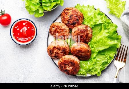 Homemade fried pork and beef meatballs with green lettuce and tomatoes, white table background, top view Stock Photo