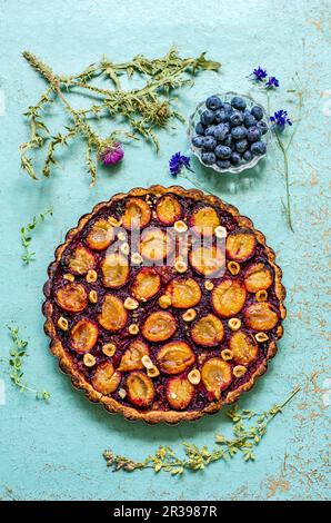 Pie with plums and hazelnuts on a blue background with herbarium and fresh blueberries Stock Photo