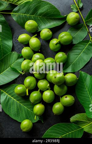 Green walnuts and walnut leaves on a black surface Stock Photo