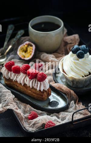 Eclair with berries and cream, and vanilla cupcake, black coffee Stock Photo