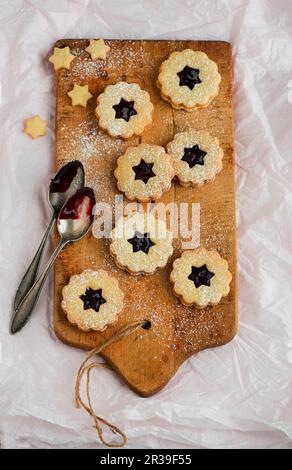 Linzer Plätzchen (nutty shortcrust jam sandwich biscuits with holes on top) on a wooden board Stock Photo