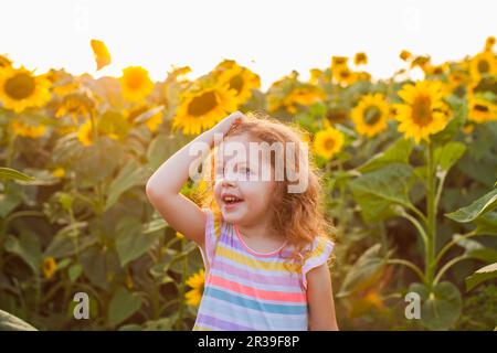 Happy daughter in sunflowers field on warm summer day. Stock Photo