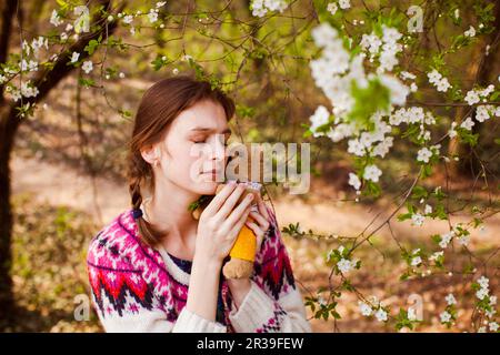 Teenage girl huggs toy bear in spring garden. Beautiful sad girl face with freckles. Stock Photo