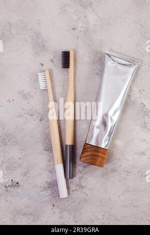 Bamboo teeth brushes and tube of toothpaste on minimalistic concrete backgroud. Zero waste concept Stock Photo