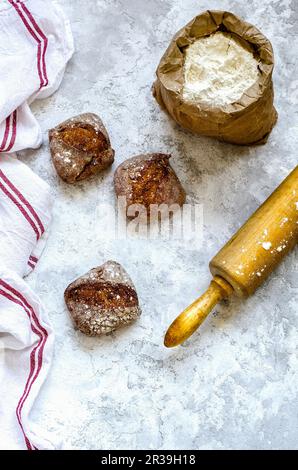 Portioned buckwheat bread, flour in a paper bag, a towel and wooden rolling pin on a concrete background Stock Photo