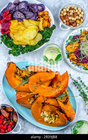 Vegan food, baked pumpkin with sage, germinated seeds and chips from two kinds of potatoes, pumpkin, beetroot and kale, dried fruits and nuts Stock Photo