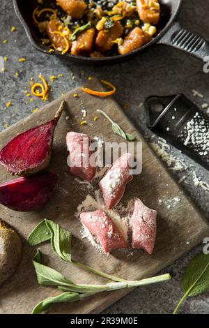 Beetroot gnocchi on a chopping board with fresh sage, raw beetroot, parmesan and cooked dish Stock Photo