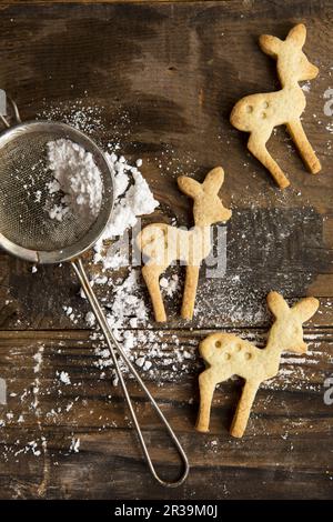 Three Festive Christmas Deer shaped cookie biscuits on a rustic board with icing sugar in a sifter Stock Photo