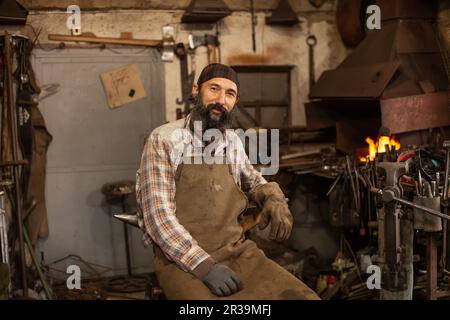 Bearded blacksmith after working in his workshop. Blacksmith's workshop. Stock Photo