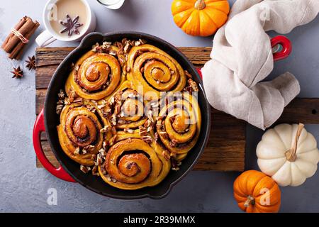 Pumpkin cinnamon rolls in a cast iron pan with nuts and sugar glaze Stock Photo