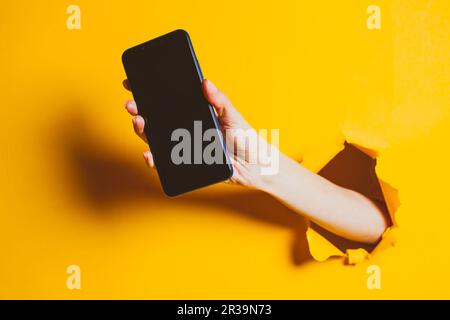 female hand out of the hole in the paper wall holding smartphone with a black screen 2r39n73