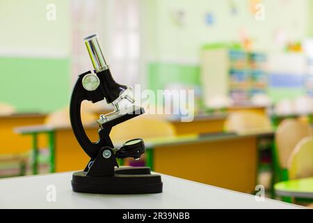 Black microscope on teachers table in empty classroom Stock Photo